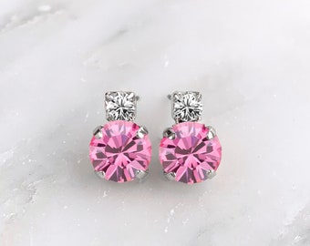 May include: A pair of silver earrings with a pink round gemstone and a smaller clear round gemstone on top.