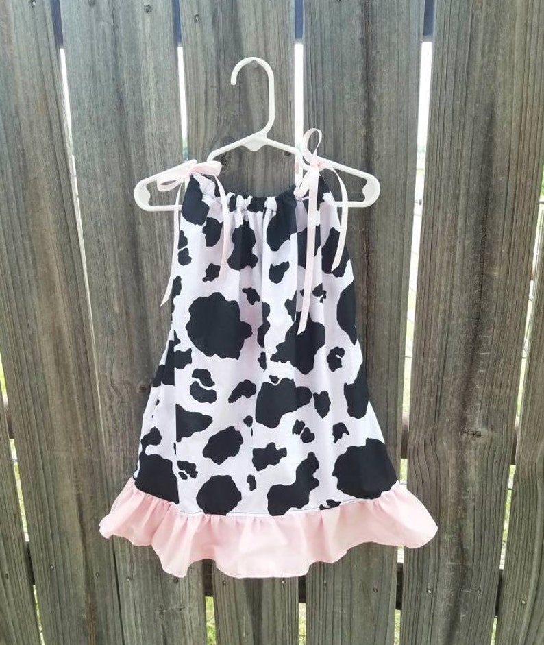 May include: A sleeveless dress with a pink ruffle hem and a black and white cow print pattern.
