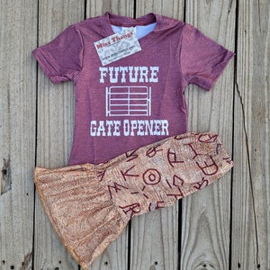May include: A maroon short-sleeved t-shirt and patterned pants set. The t-shirt features the text "FUTURE GATE OPENER" in white. The pants have a tan and maroon pattern. A tag from "Miss Thangz" is attached to the shirt.