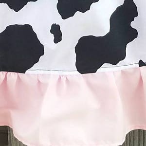 May include: A black and white cow print skirt with a pink ruffled trim.
