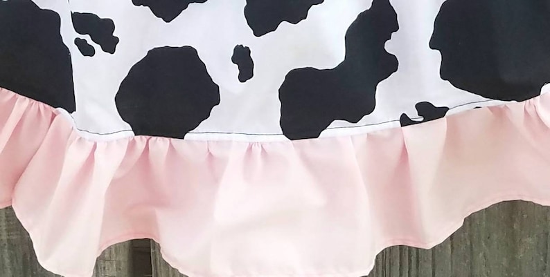May include: A black and white cow print skirt with a pink ruffled trim.