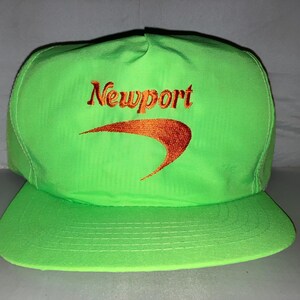 Op de afbeelding: Een neon-groene baseballpet met een gebogen oranje logo en het woord "Newport" in oranje geborduurd op de voorkant.