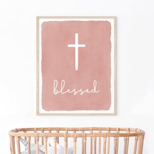 May include: A blush pink watercolor print with a white cross and the word "blessed" in white script.