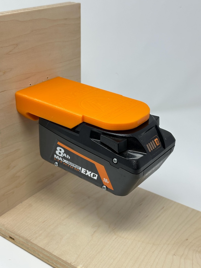 Wall mount battery holder compatible with Ridgid 18V batteries, 3D-printed organizer for workshop or garage. Durable 3D-printed wall mount for Ridgid 18V power tool batteries, easy-install storage bracket. Ridgid 18V battery wall holder and organizer, heavy-duty plastic mount for secure tool battery storage. Compact Orange wall-mounted rack designed to hold Ridgid 18V lithium power tool batteries. Space-saving Ridgid 18Vbattery mount for workshop walls, keeps batteries organized.