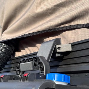 May include: A black plastic water tank with a blue cap, a black handle, and a black metal bracket attached to a gray canvas tent.