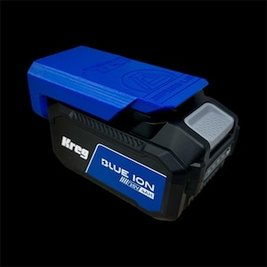 Pode incluir: Uma bateria Kreg Blue Ion 20V 4AH azul e preta. A bateria tem uma parte superior azul e um corpo preto com os logotipos Kreg e Blue Ion. A bateria é projetada para ferramentas elétricas.