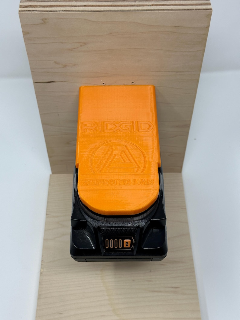 Wall mount battery holder compatible with Ridgid 18V batteries, 3D-printed organizer for workshop or garage. Durable 3D-printed wall mount for Ridgid 18V power tool batteries, easy-install storage bracket. Ridgid 18V battery wall holder and organizer, heavy-duty plastic mount for secure tool battery storage. Compact Orange wall-mounted rack designed to hold Ridgid 18V lithium power tool batteries. Space-saving Ridgid 18Vbattery mount for workshop walls, keeps batteries organized.