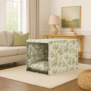 May include: A black wire dog crate with a green and white toile fabric cover and matching bed. The crate is placed on a cream-colored rug in a living room setting. The fabric features a scenic design.