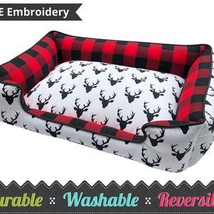 May include: Red and black buffalo plaid dog bed with a white deer print on the inside. The bed is reversible and has a black border. The text "FREE Embroidery" is on a black ribbon at the top of the image. The text "Durable Washable Reversible" is at the bottom of the image.
