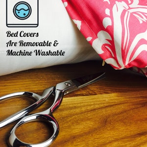 May include: A close-up of a white pillow with a pink and white patterned pillowcase. The image includes a pair of silver scissors and text that reads "Bed Covers Are Removable & Machine Washable" with a washing machine icon.