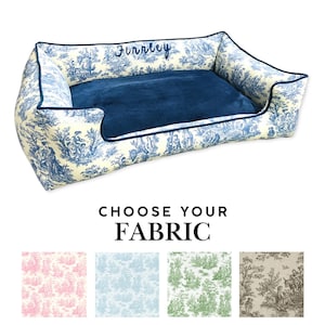 May include: A white and blue patterned dog bed with a blue velvet insert. The bed is personalized with the name "Funnley". Choose from four fabric options: pink, blue, green, and brown.