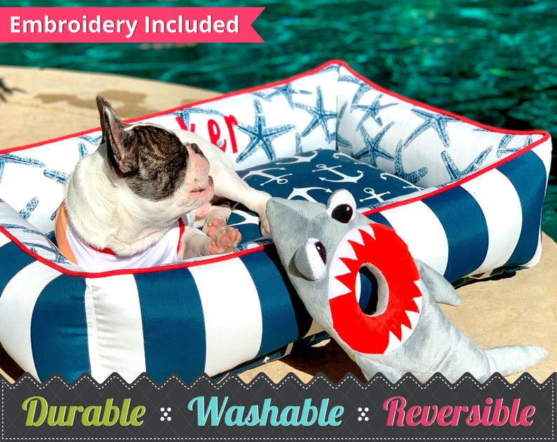 Nautical Pet Bed & Frenchie dog sitting by a pool, with shark stuffed toy close by.