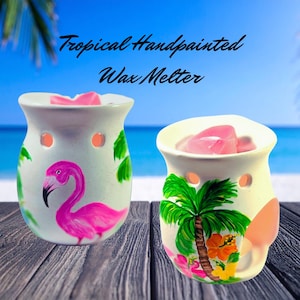 May include: Two hand-painted ceramic wax melters with tropical designs. One features a pink flamingo, the other a palm tree and flowers. The text "Tropical Handpainted Wax Melter" is above the melters.