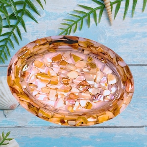 May include: Oval-shaped soap dish with a mosaic design. The dish is filled with small, irregularly shaped pieces in shades of gold, beige, and brown. The dish has a clear, glossy finish, and the mosaic pieces are embedded in a clear resin.