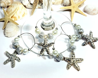 May include: Set of four silver and white glass charms featuring a starfish design. Each charm has a pearl and sparkly beads.
