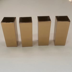 May include: Four gold-coloured metal square candle holders.
