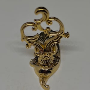 May include: A gold-colored metal decorative stand with a swirling, ornate design. The stand has a round base and a tall, intricate top.