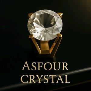 Puede incluir: Un gran cristal transparente engastado en un marco dorado. El cristal está sobre una superficie negra con el texto "ASFOUR CRYSTAL" en letras doradas.