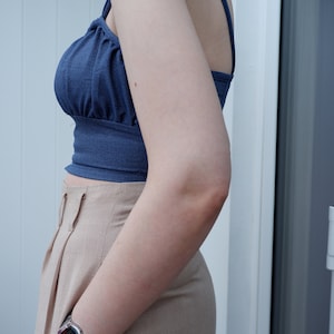 Pu&ograve; includere: Una donna indossa un top corto blu con un paio di pantaloni beige a vita alta. Indossa un orologio digitale al polso sinistro.