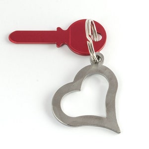 May include: A red key with a silver heart-shaped keychain. The key has a round head and a silver ring.