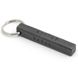 Könnte beinhalten: Ein silberner Schlüsselring, der an einem schwarzen Metallstab befestigt ist, auf dem die Namen "Robert" und "Carol" eingraviert sind.
