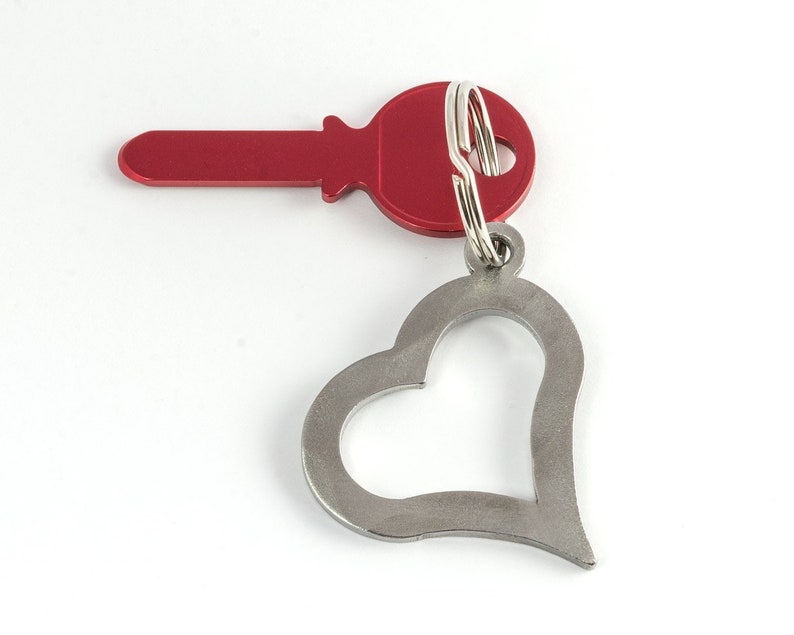 May include: A red key with a silver heart-shaped keychain. The key has a round head and a silver ring.
