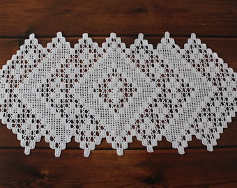 May include: A white rectangular crochet table runner featuring an intricate geometric diamond pattern with openwork lace details and a scalloped edge. The textile is crafted with fine thread, showcasing a repeating symmetrical design throughout.