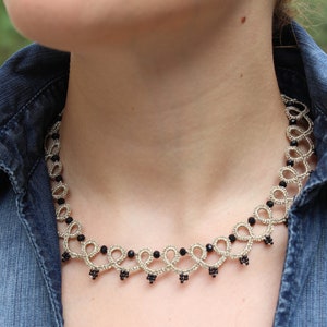 May include: A silver and black beaded necklace with a delicate, intricate design. The necklace is worn by a person with a denim shirt.