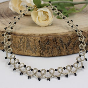 May include: A delicate silver-colored necklace with black beads, featuring a looped design. The necklace is displayed on a wooden surface.