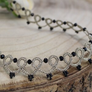 May include: A silver and black beaded choker necklace with a delicate, intricate design. The necklace is made of a thin, braided cord with small black beads interspersed throughout.