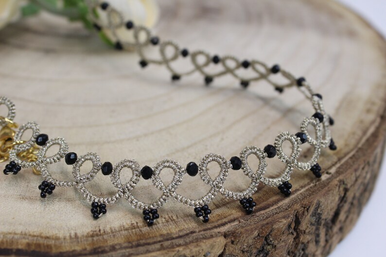 May include: A silver and black beaded choker necklace with a delicate, intricate design. The necklace is made of a thin, braided cord with small black beads interspersed throughout.