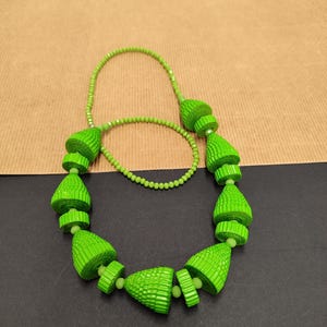 May include: A bright green necklace with cone-shaped beads and a beaded chain. The necklace features a series of textured, cone-shaped beads in a vibrant green color, connected by a delicate beaded chain. The necklace is displayed against a neutral background.