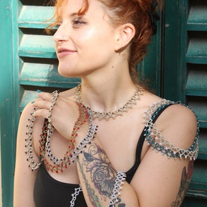 May include: A woman wearing a black tank top with a tattoo on her arm. She is wearing multiple silver, black, and red beaded necklaces and bracelets.