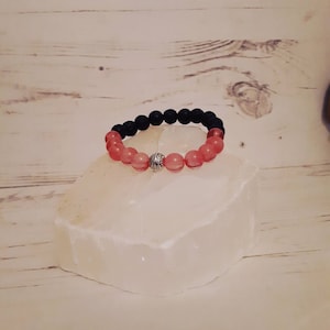 May include: A black lava rock and pink rose quartz beaded bracelet with a silver charm.