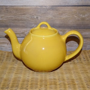 May include: A yellow ceramic teapot with a round body and a lid. The teapot has a handle on the side and a spout on the front.