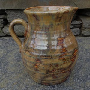 May include: A brown ceramic pitcher with a mottled glaze. The pitcher has a wide mouth and a handle.