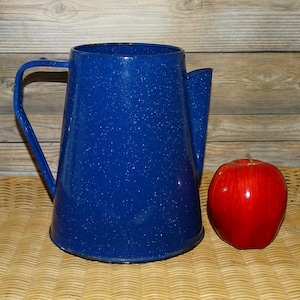 May include: Blue enamel coffee pot with a speckled finish and a handle. The pot is sitting on a woven surface.