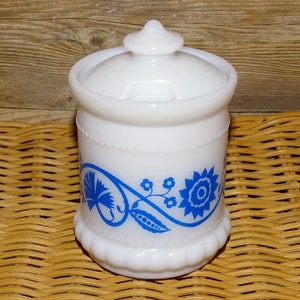 May include: White milk glass jar with a blue floral design. The jar has a white lid with a knob on top.