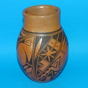 May include: A brown pottery vase with a wide body and a narrow neck. The vase is decorated with black geometric patterns, including triangles, lines, and star-like shapes. The background is a solid blue.