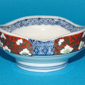 May include: A small, white ceramic bowl with a blue and red floral design. The bowl has a scalloped rim and a raised base.