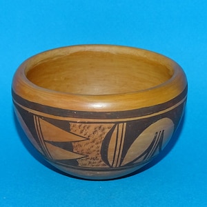 May include: A small, brown ceramic bowl with black geometric designs. The bowl is round and has a slightly flared rim.