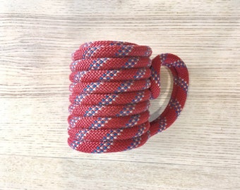 May include: A red and blue rope mug. The rope is coiled to form the mug shape, with a handle made of the same rope.