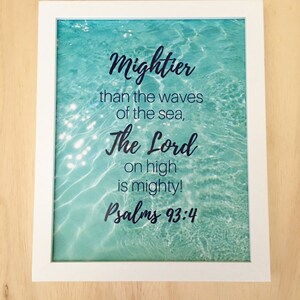 May include: A framed print with a blue and green water background. The print features a quote from Psalms 93:4, "Mightier than the waves of the sea, The Lord on high is mighty!"