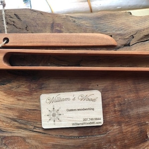 Puede incluir: Un juego de pinzas de madera y una espátula de madera, ambas con un acabado de madera natural. Las pinzas miden 30 cm de largo y la espátula 25 cm de largo. El juego está hecho por William's Wood, un negocio de carpintería personalizado.