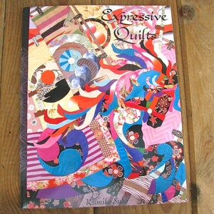May include: A book titled "Expressive Quilts" by Kumiko Sudo. The cover features a colorful abstract design with a mix of red, blue, pink, and yellow fabrics.