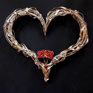 May include: A gold metal heart-shaped wreath with a cluster of three red roses in the center.