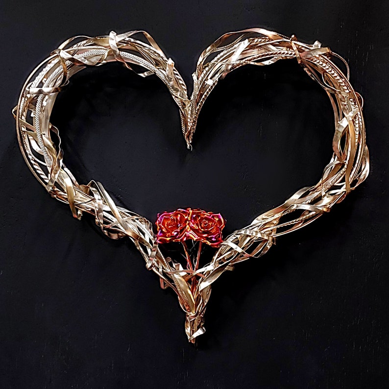 May include: A gold metal heart-shaped wreath with a cluster of three red roses in the center.