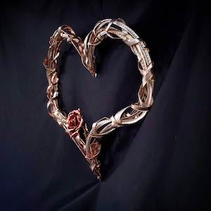 May include: A gold metal heart-shaped wreath with a single red rose attached to the bottom.