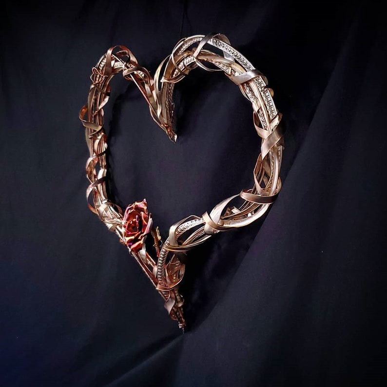 May include: A gold metal heart-shaped wreath with a single red rose attached to the bottom.