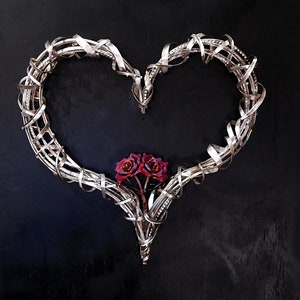 May include: A silver metal heart-shaped wreath with two red roses in the center.
